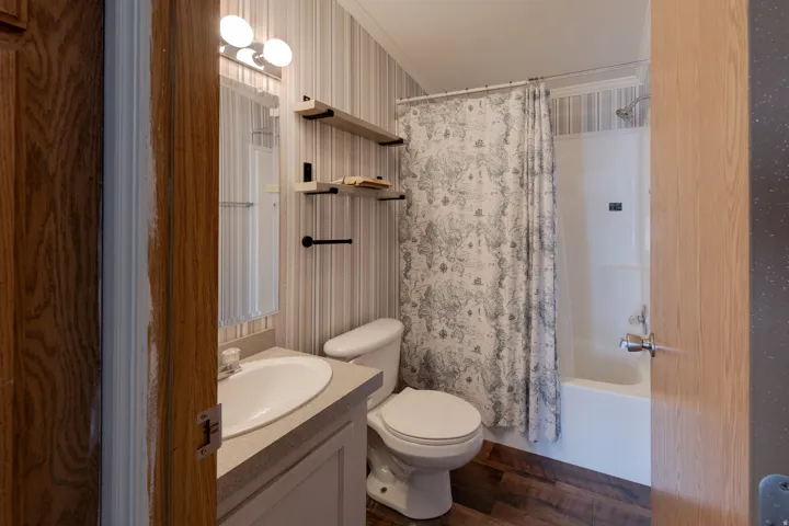 Wood-finish flooring, single vanity with integrated sink, wall-mounted mirror, built-in shelving, and a tub/shower combination
