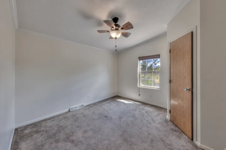 Crown molding details, ceiling fan with integrated lighting, wood-finish door, and carpeted flooring
