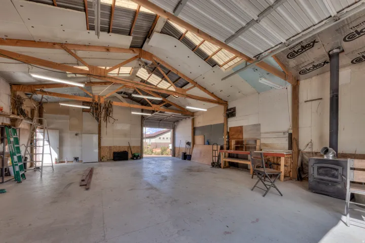 Spacious interior featuring exposed wooden beam construction, a metal roof with multiple skylights, and fluorescent lighting fixtures