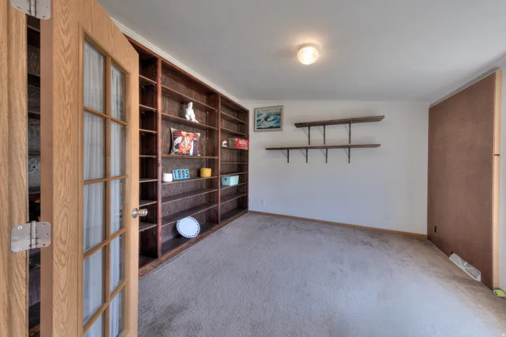 Built-in shelving, glass-paned interior door, wall-mounted floating shelves, and carpeted flooring