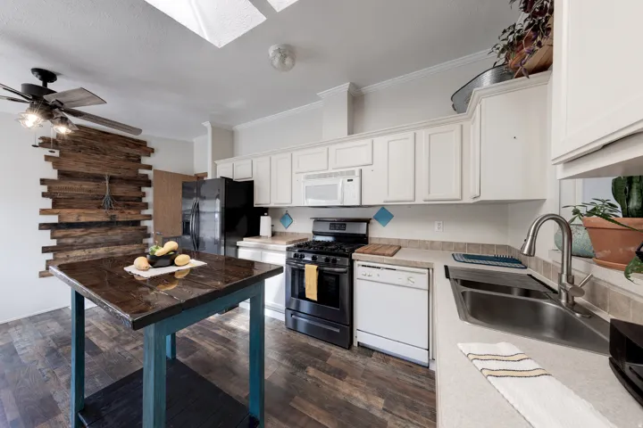 Kitchen featuring white cabinetry, wood-finish flooring, a stainless steel sink, and a black gas range