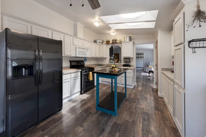 Wood-finish flooring throughout, white cabinetry with crown molding, black appliances, and a skylight
