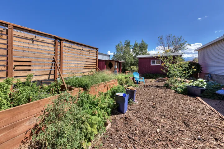 Expansive backyard featuring multiple raised garden beds, wood chip ground cover, and a wood privacy fence