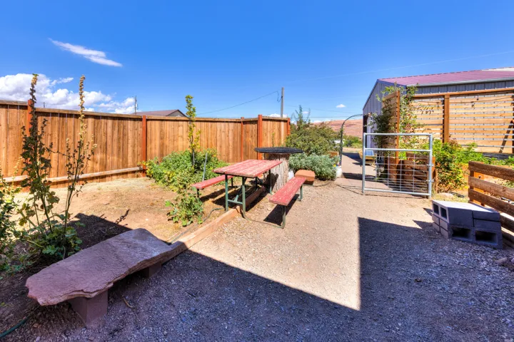 Gravel patio area with a wooden fence boundary, featuring a picnic table and a stone bench