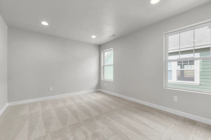 Recessed ceiling lighting, light gray wall paint, two windows, and patterned carpeting