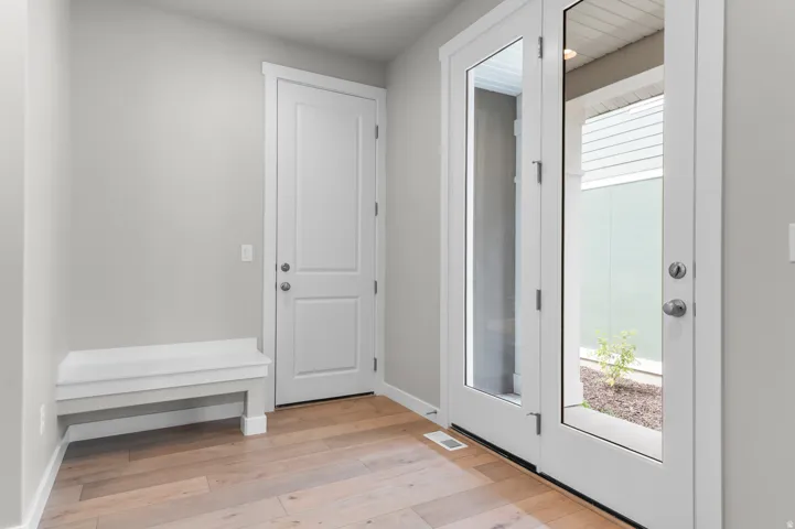 Wood-finish flooring with a light tone, white built-in bench, white interior door, and white French doors with clear glass panels