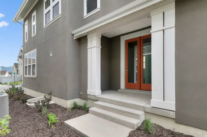Stucco exterior, covered front entry, double-panel glass doors, concrete steps, and landscaped planting areas