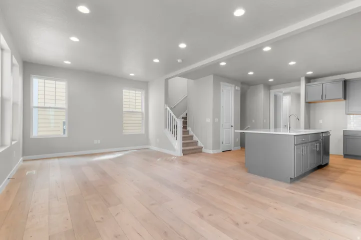 Light wood-finish flooring, recessed ceiling lighting, light gray painted walls, a kitchen island with gray cabinetry, and a carpeted staircase