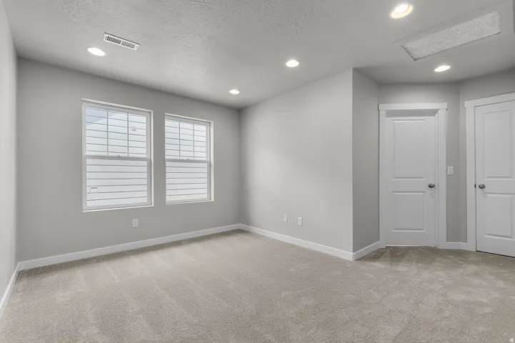 Neutral wall paint, two white paneled doors, recessed ceiling lighting, two windows with white blinds, and gray carpeting