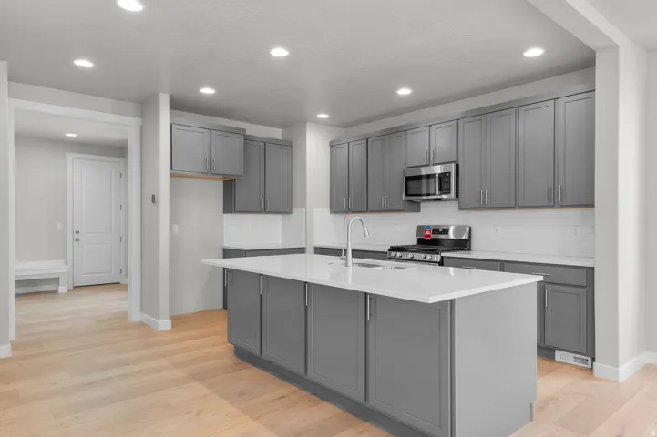 Kitchen featuring light wood-finish flooring, gray cabinetry, white countertops, stainless steel appliances, and a white subway tile backsplash