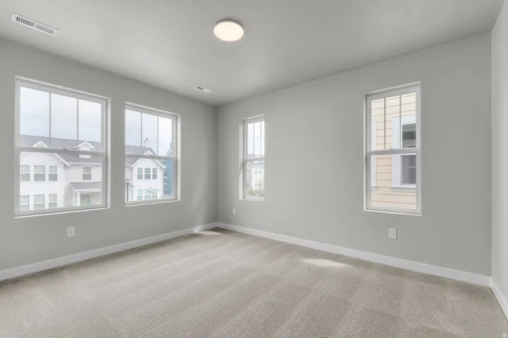 Neutral paint tones throughout, featuring light-colored carpeting, multiple windows with white trim, and a ceiling-mounted light fixture