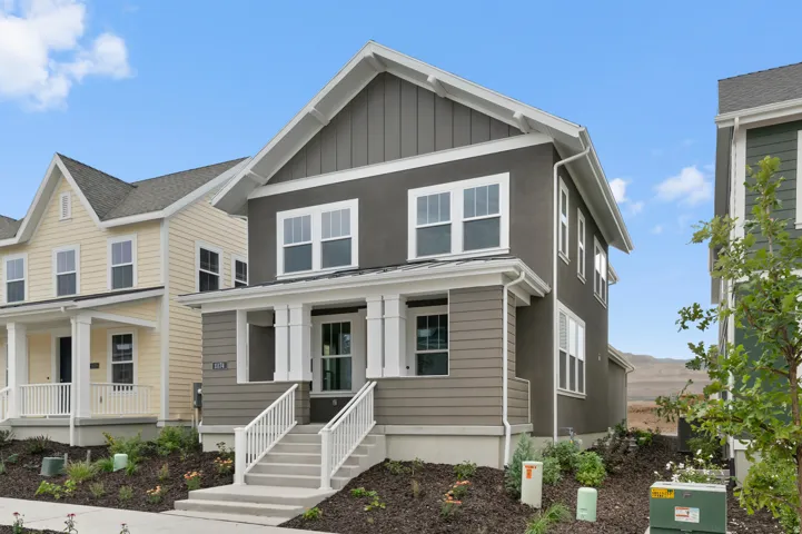 Two-story exterior featuring a gray stucco and siding finish, white trim, a gabled roofline, and a prominent entry porch with white railings