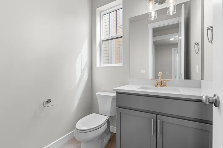 Bathroom featuring a gray vanity with an integrated sink, gold-toned faucet, wall-mounted mirror, and overhead light fixture