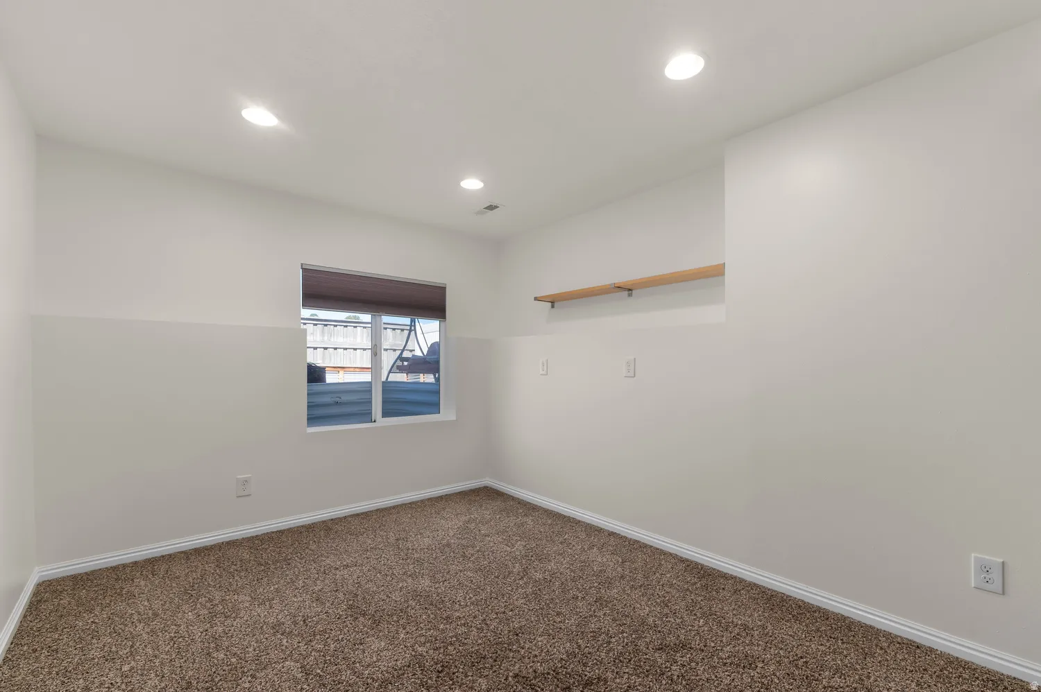 Neutral wall paint, brown carpet flooring, recessed lighting, white window trim, and a built-in wooden shelf