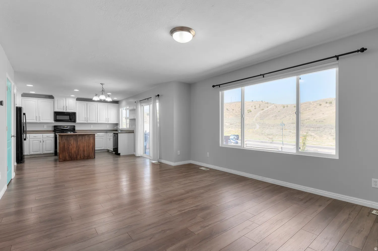Open-concept living area with wood-finish flooring, white kitchen cabinetry, a dark wood-finish island, and large windows providing a mountain backdrop