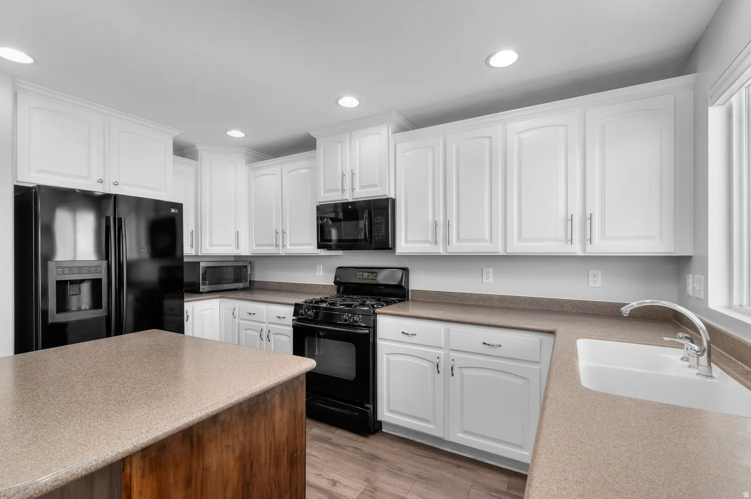 Kitchen featuring white cabinetry, dark wood-finish flooring, a central island with a light-toned countertop, and a white farmhouse sink