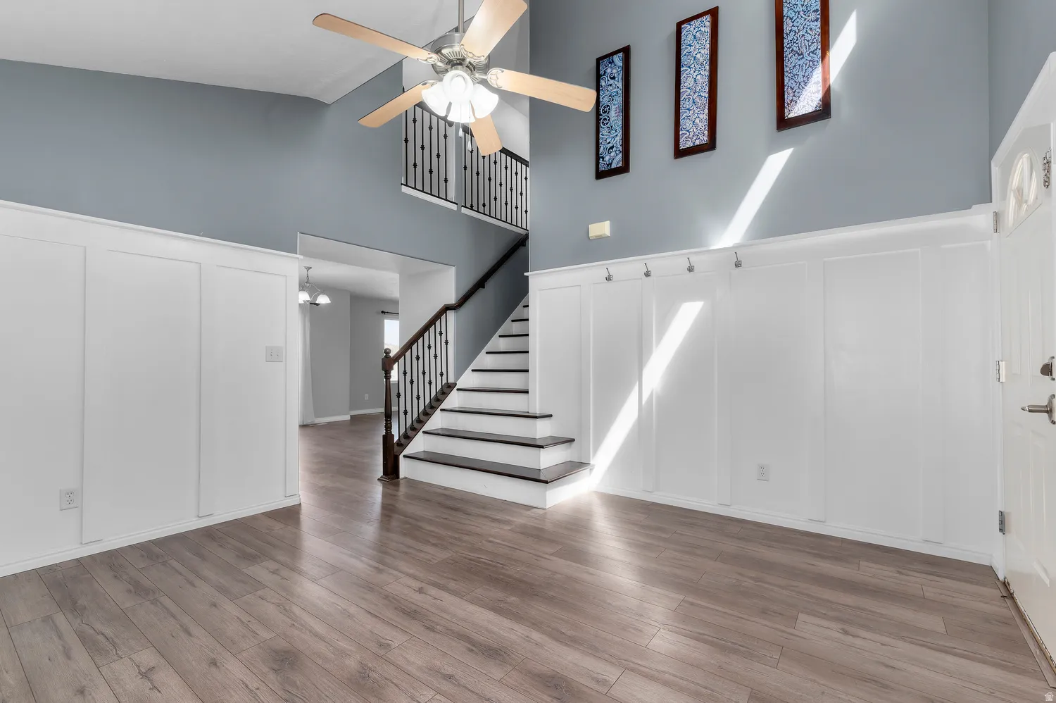 Wood-finish flooring, high ceilings, board and batten wall detailing, staircase with black balusters, and a ceiling fan