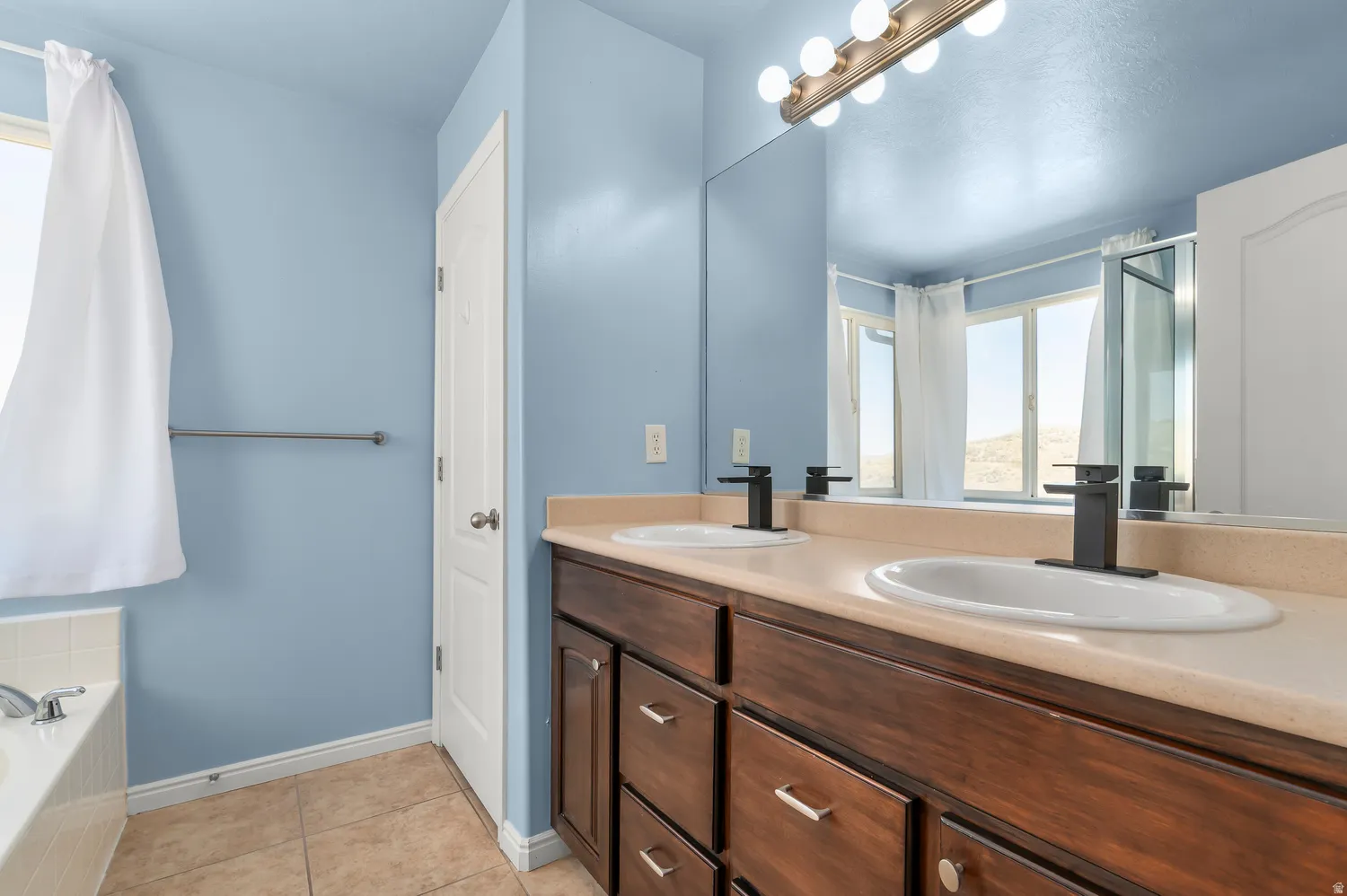 Master-Dual vanity with dark wood-finish cabinetry, white oval undermount sinks, and matte black faucets
