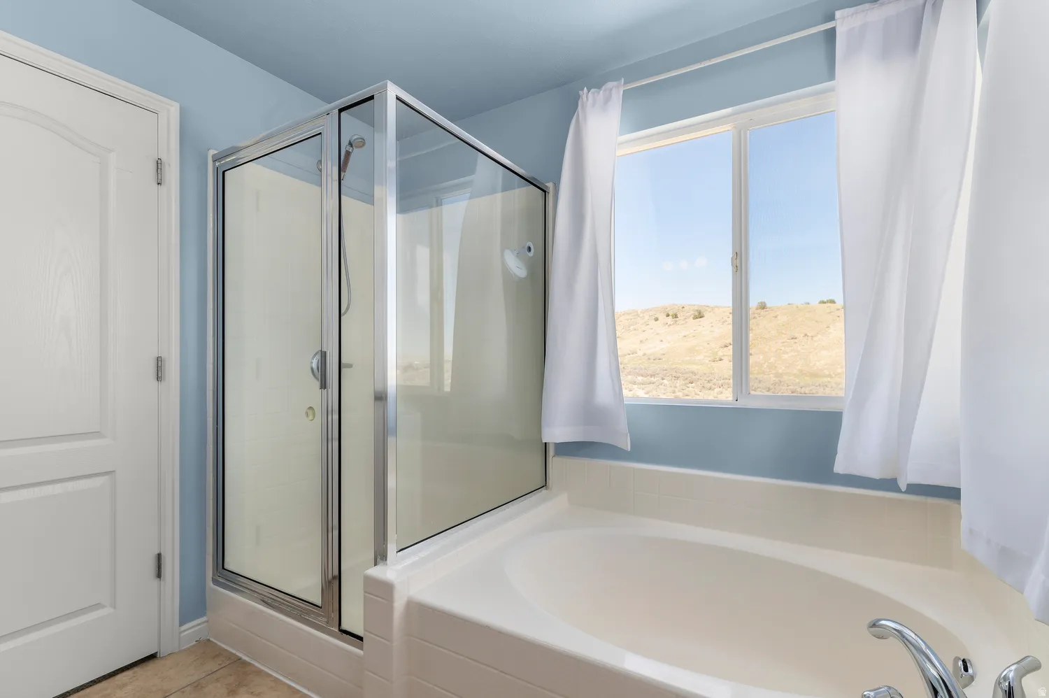Master-Soaking tub with chrome fixtures, glass-enclosed shower, large window, and light blue walls
