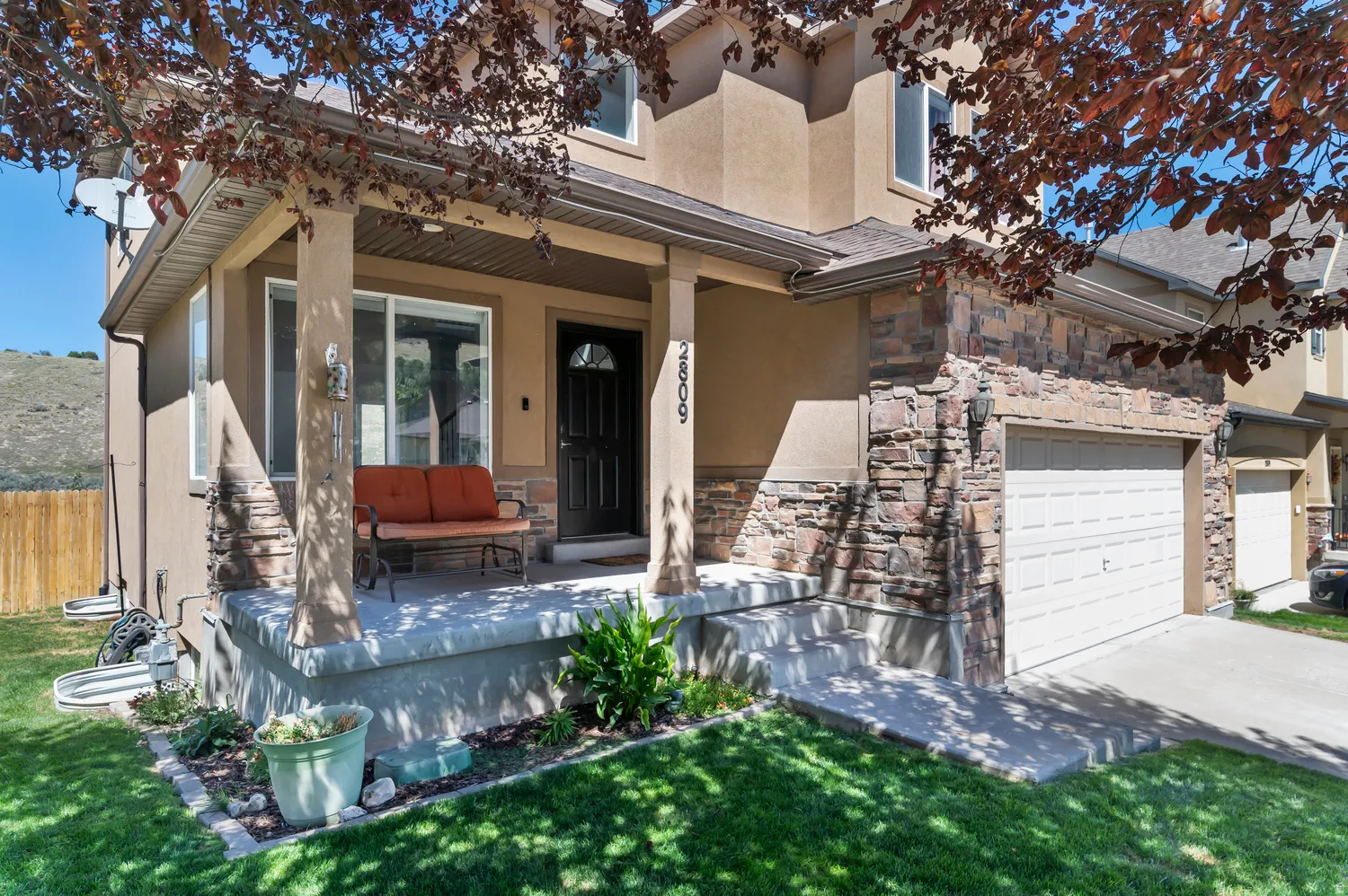 Covered porch with stone column accents, stucco exterior, stone facade, and attached garage