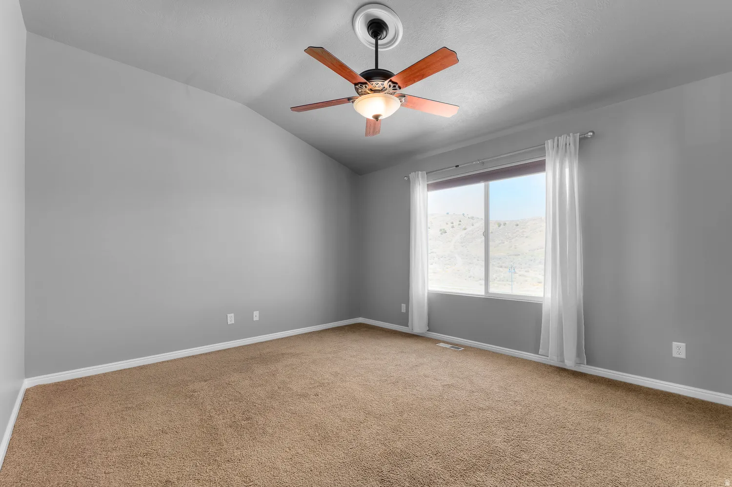 Primary Bedroom-Vaulted ceiling, ceiling fan with light fixture, large window with ample natural light, brown carpeting, and light gray wall finish