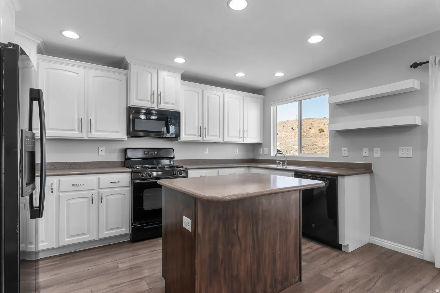 Kitchen featuring white cabinetry, black appliances, a central island, wood-finish flooring, and recessed lighting