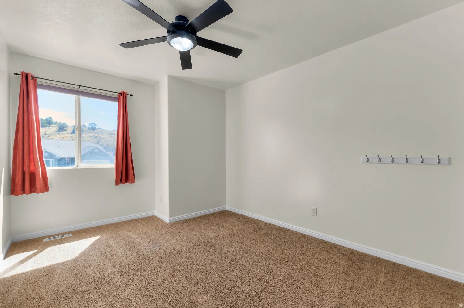 Carpeted room featuring a ceiling fan with integrated lighting, a window with a mountain backdrop, and a wall-mounted hook rack