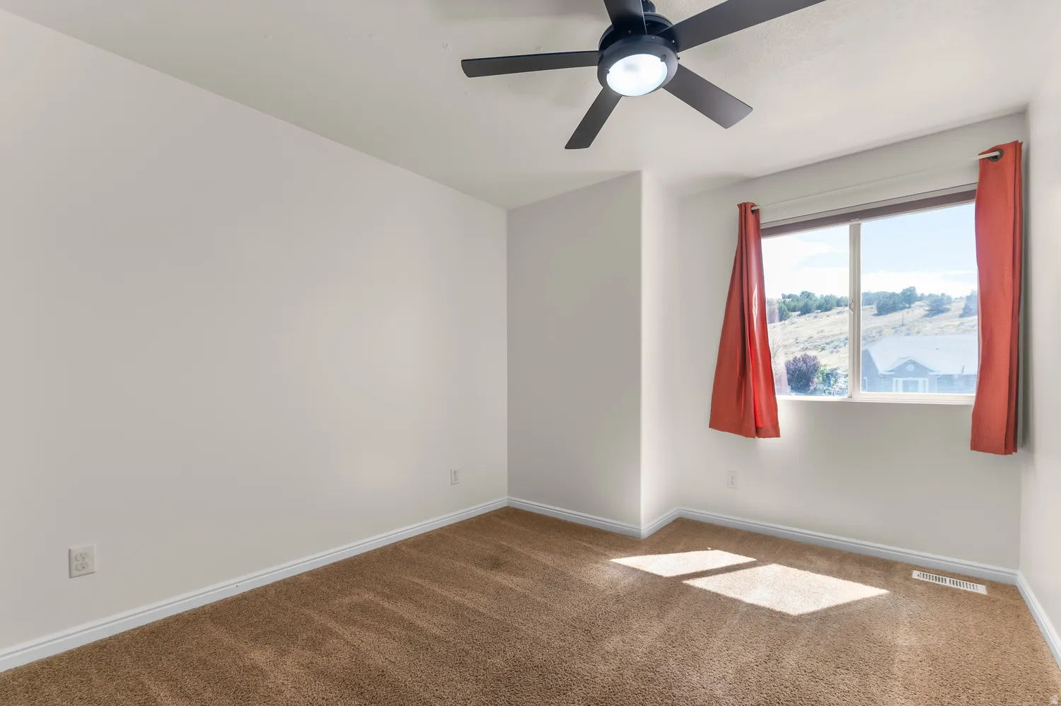 Neutral wall paint, brown carpeting, a window, and an overhead ceiling fan with light