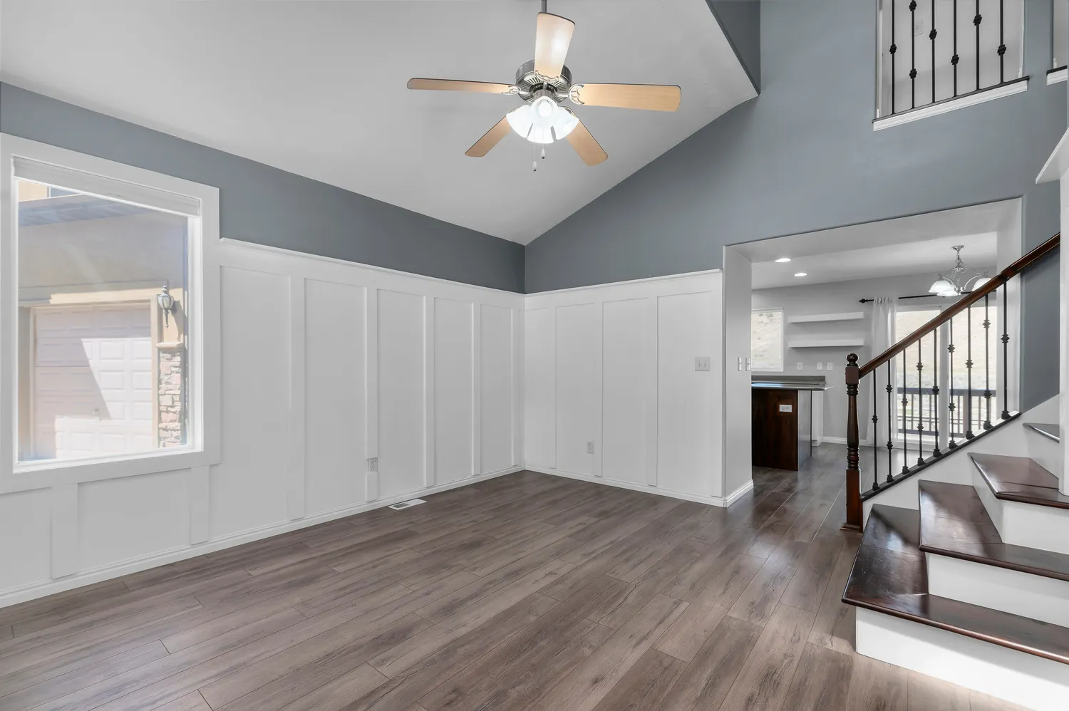 Vaulted ceiling with a ceiling fan, board-and-batten wall detailing, wood-finish flooring, and a staircase with dark wood treads and an iron baluster railing