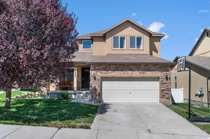 Two-story residence featuring a two-car garage, stone and stucco exterior, front porch, and mature landscaping