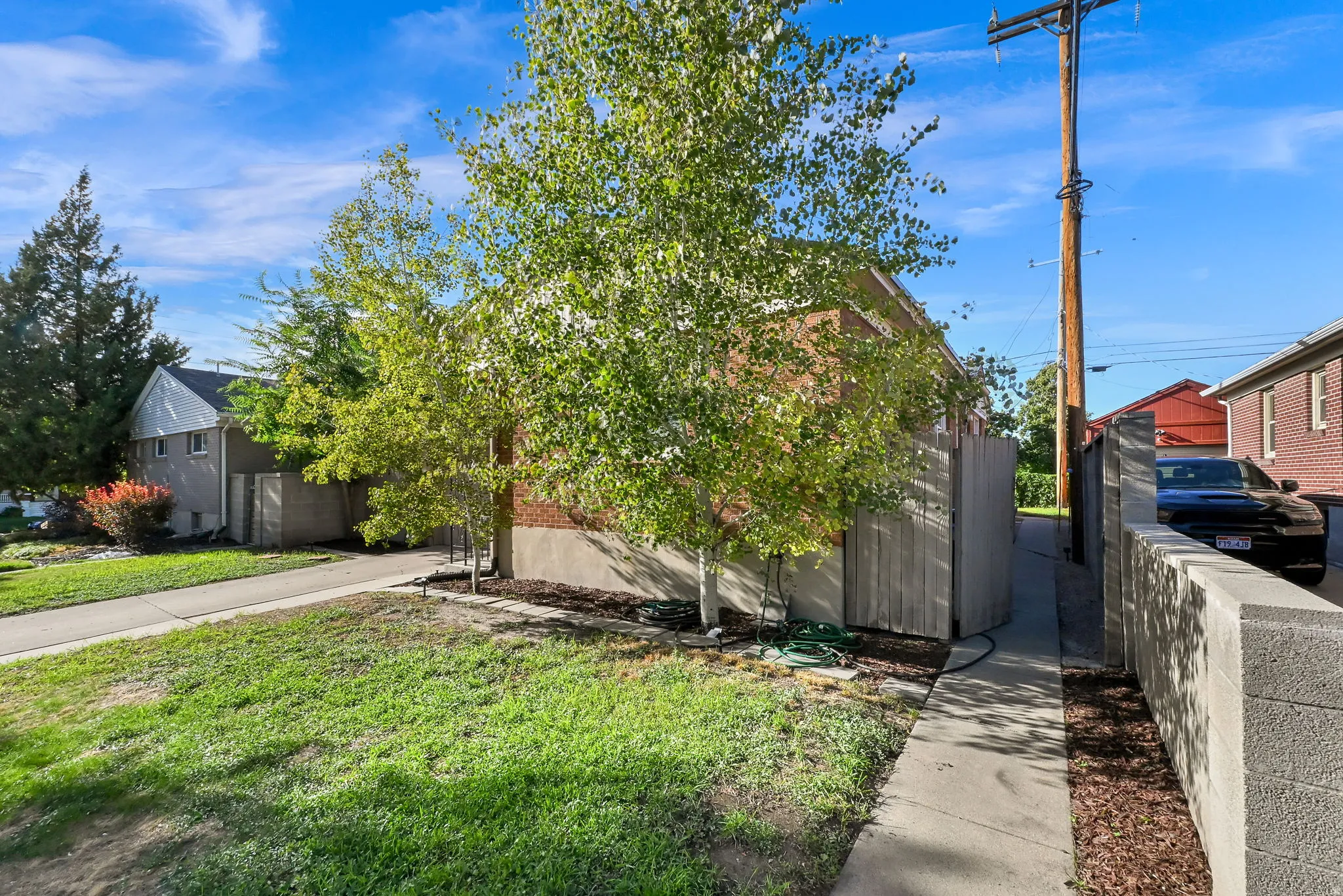Brick facade with mature trees, a concrete walkway, and a concrete block retaining wall
