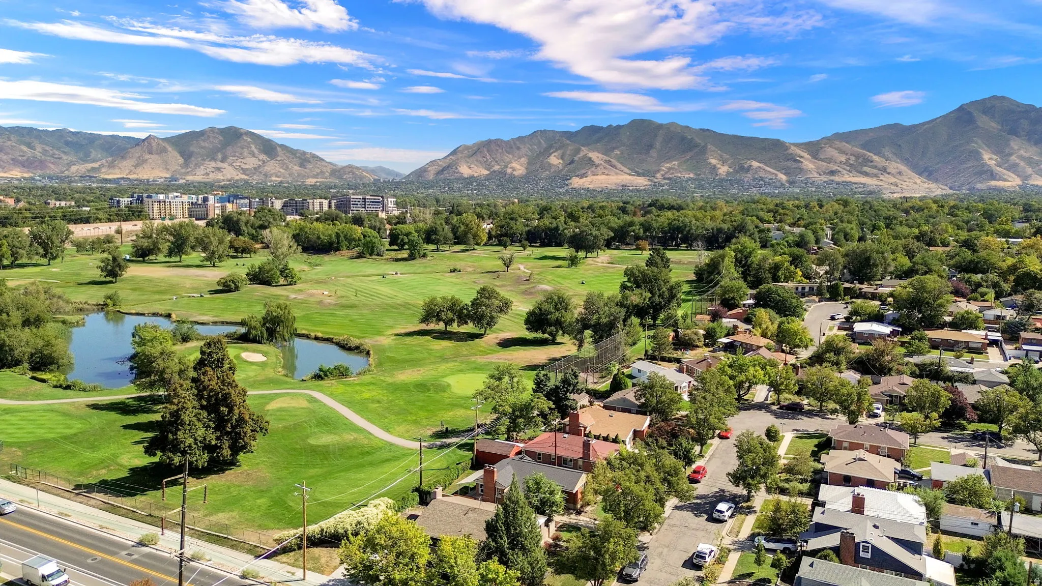 Expansive green space featuring a golf course, mature trees, and water features, framed by distant mountains and surrounding residential properties