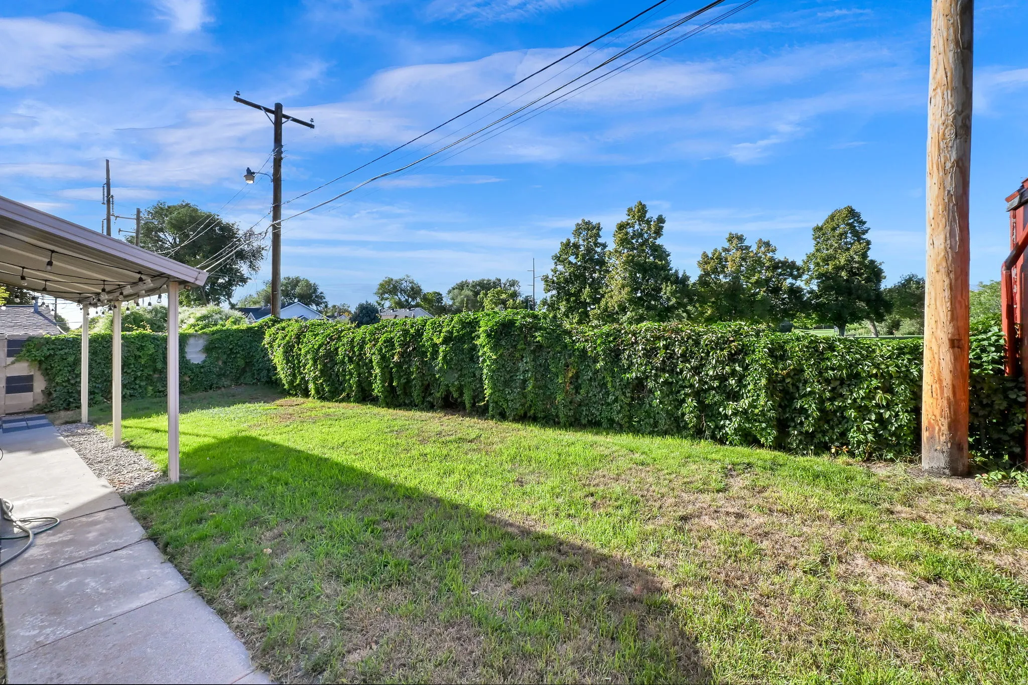 Expansive grassy yard with a manicured hedge, concrete patio, and covered outdoor area