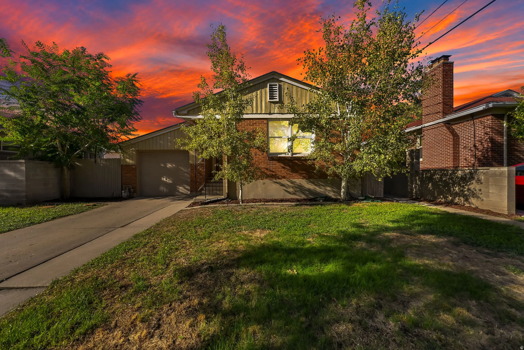 Brick and siding facade, attached garage, mature trees, concrete driveway, and front lawn