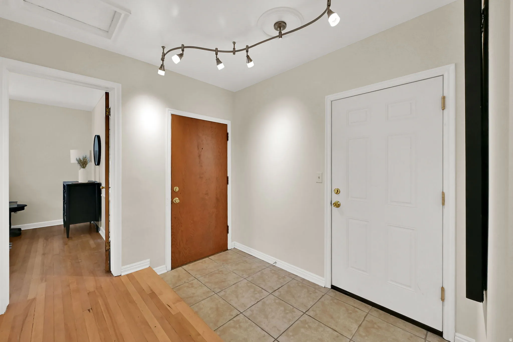 Tiled flooring, overhead track lighting, wood-finish flooring, white paneled door, wood-finish door