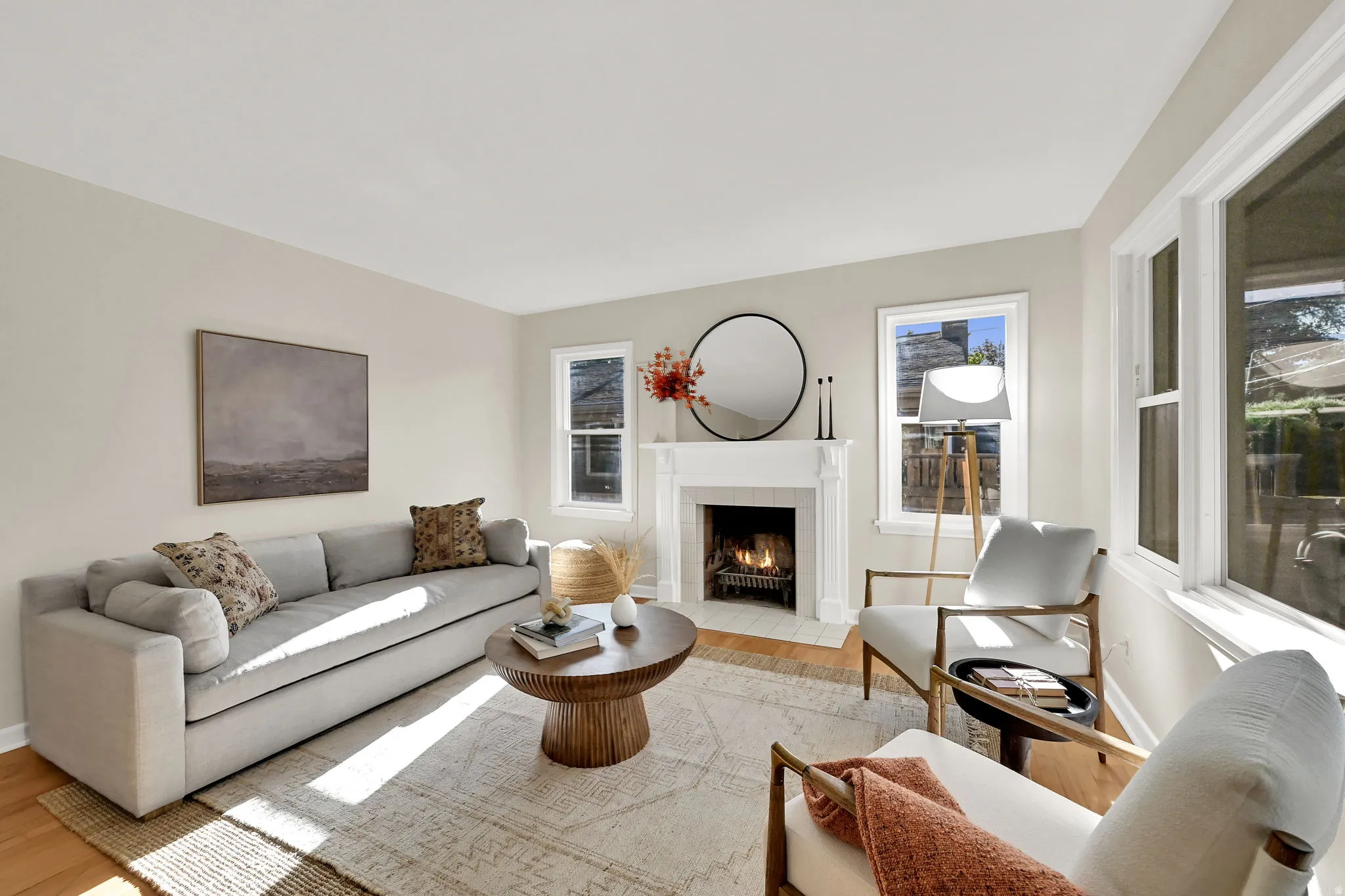 Hardwood-style flooring throughout, white fireplace with hearth and mantel, multiple windows, and light-toned walls