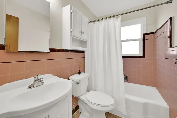 Bathroom featuring a vanity with an integrated sink, white storage cabinetry, and tiled walls surrounding the tub