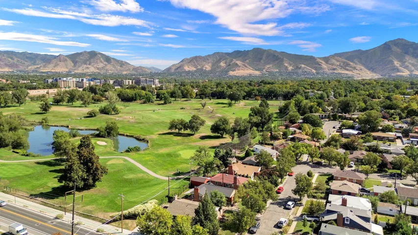 Expansive green space featuring a golf course, mature trees, and water features, framed by distant mountains and surrounding residential properties