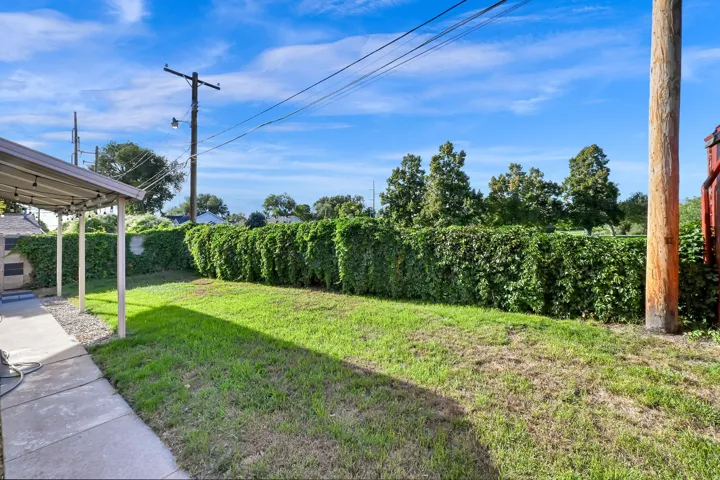 Expansive grassy yard with a manicured hedge, concrete patio, and covered outdoor area
