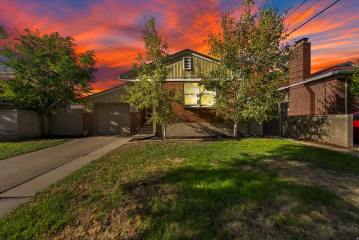 Brick and siding facade, attached garage, mature trees, concrete driveway, and front lawn