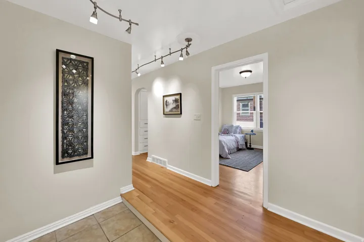 Hardwood flooring, track lighting, neutral wall tones, arched entryway, and a built-in recessed storage unit