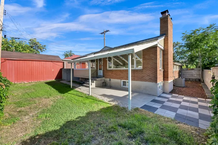 Brick exterior featuring a covered patio, a checkered stone patio area, and a red-sided detached outbuilding