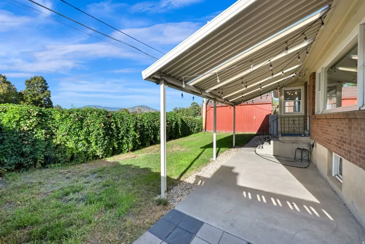 Covered patio with a concrete surface, mature privacy hedging, and expansive yard space