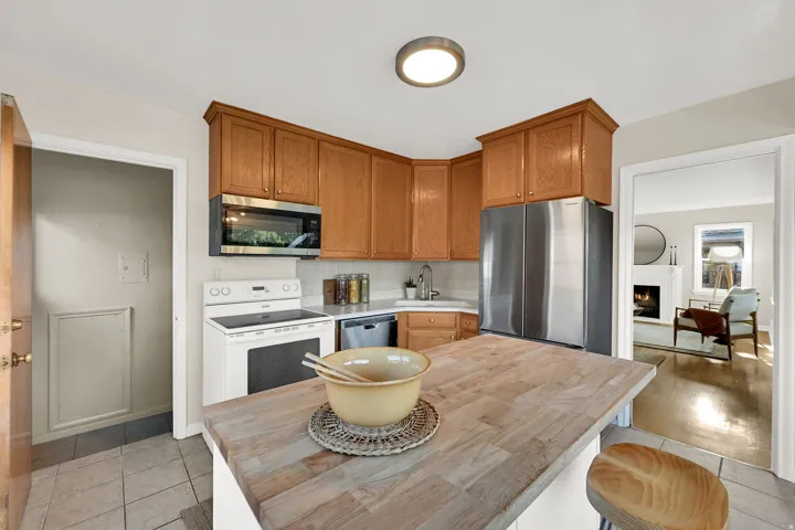Kitchen featuring wood cabinetry, stainless steel appliances, a wood-finish island countertop, and tile flooring