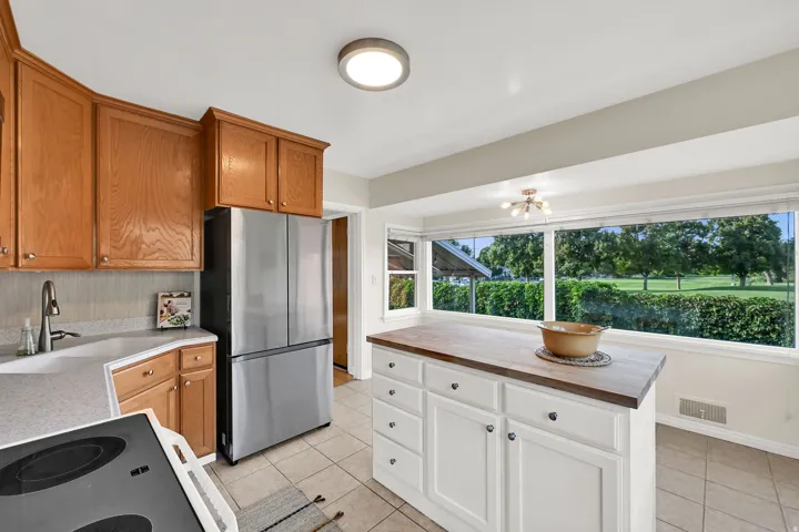 Kitchen featuring warm wood cabinetry, a stainless steel refrigerator, a center island with a wood-finish countertop, and large windows with exterior green space