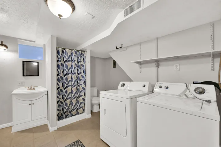 Dedicated laundry area with a full-size washer and dryer, adjacent to a vanity sink with cabinet storage, and a shower with a patterned curtain