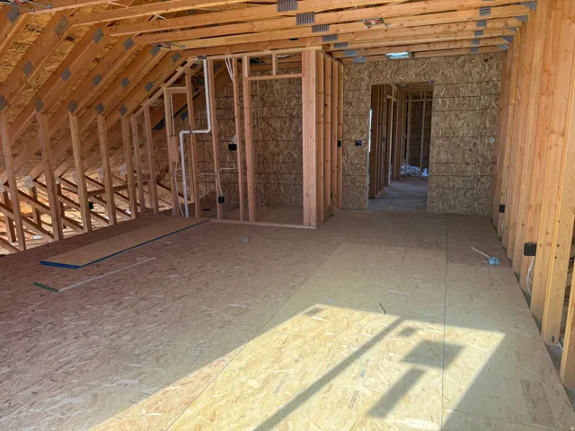 Unfinished attic space featuring exposed wood framing, oriented strand board walls, and subflooring
