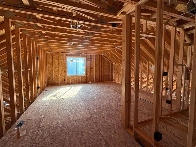 Spacious unfinished attic space featuring exposed wood framing, a single window, and subflooring