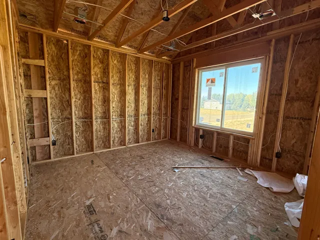 Unfinished room with exposed wood framing, plywood subfloor, and a large window