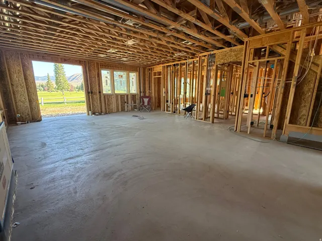 New construction framing with exposed ceiling joists, concrete flooring, and multiple window openings